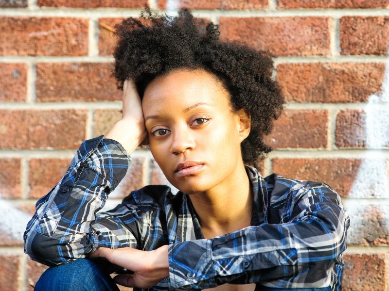 Black woman looking at dry, natural hair in the shower.