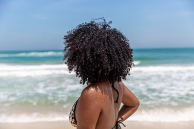 Black woman with natural curly hair in front of the ocean.
